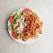 A white plate filled with a serving of doner kebab meat, fresh sliced tomatoes, cucumber, and lettuce, accompanied by creamy white and red sauces.