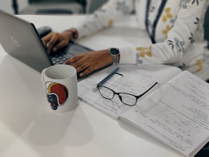 A person working on a laptop with notes and a cup of coffee nearby.
