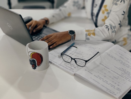 A person working on a laptop with notes and coffee nearby in a cozy workspace.