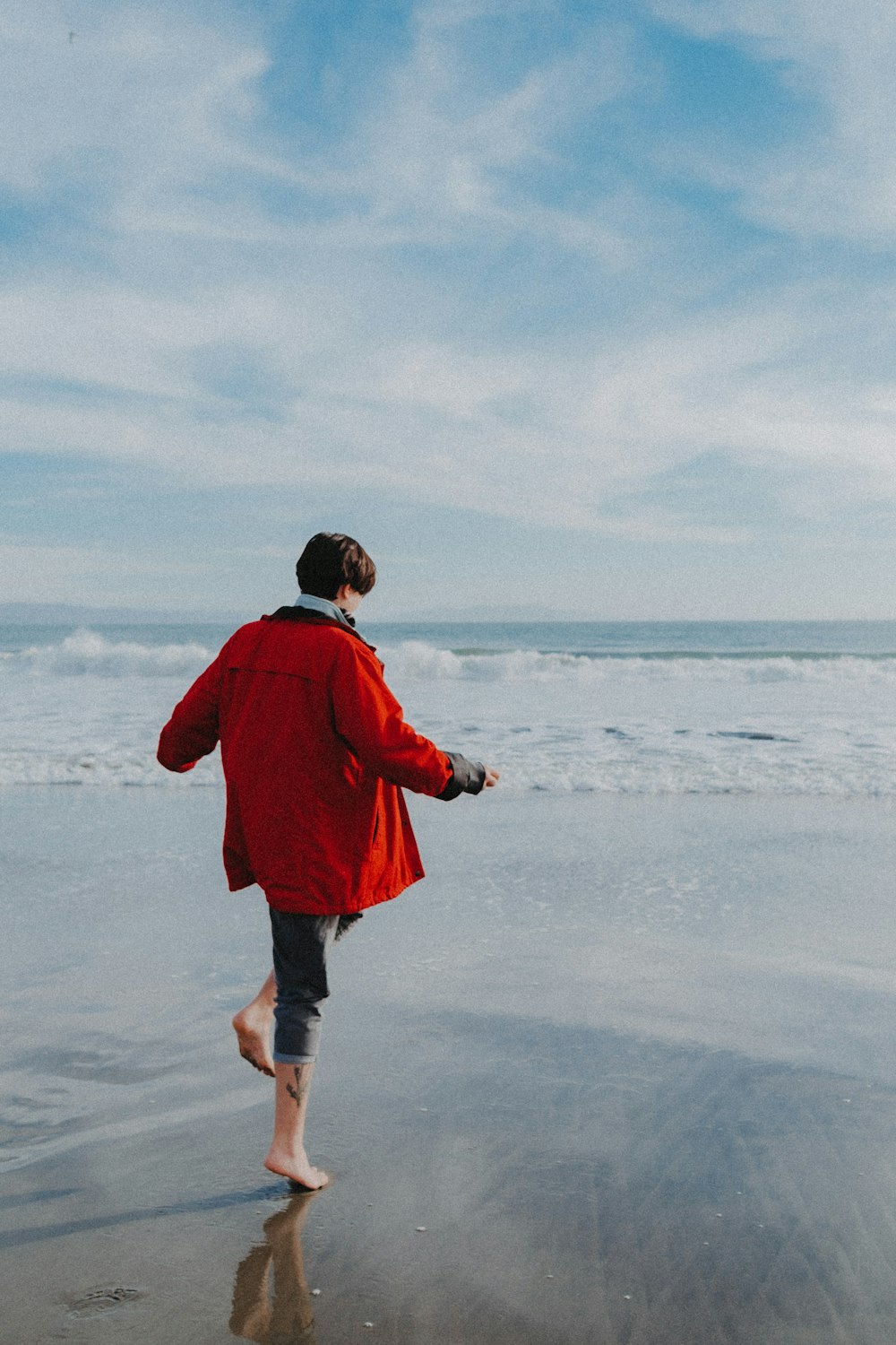 a woman in a red coat is walking on the beach