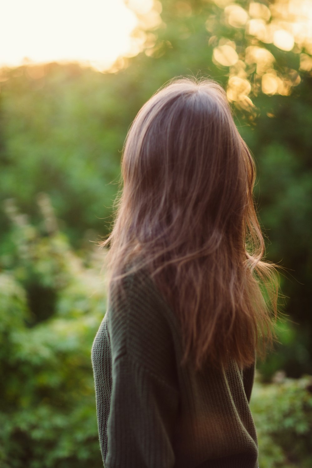 a woman with long hair standing in front of trees