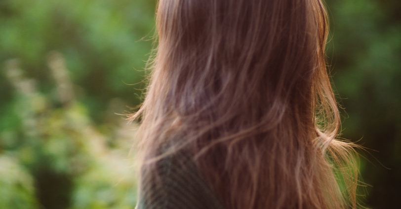 a woman with long hair standing in front of trees