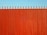 A tall, vertical red fence with evenly spaced slats and pointed tops stands against a clear blue sky.