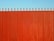 A tall, vertical red fence with evenly spaced slats and pointed tops stands against a clear blue sky.
