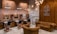 A stylish barbershop interior featuring brick walls adorned with vintage signs and a prominent Route 66 theme. There are multiple barber stations with mirrors and black cushioned chairs featuring copper accents. The seating area includes brown tufted leather sofas and chairs. Modern lighting fixtures and exposed copper piping add an industrial touch to the cozy ambiance.
