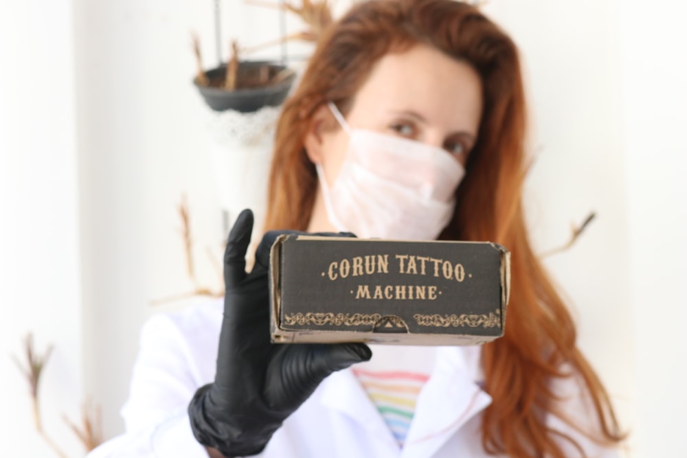 a woman in a white lab coat and black gloves holds up a box with a