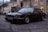A classic black sedan is parked on a cobblestone street beside a row of buildings with yellow and beige facades. The car has a sleek, vintage design with chrome accents and a visible license plate reading WW 445XC.