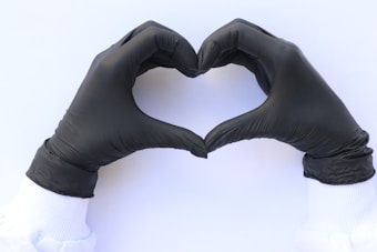 Two hands wearing black gloves form a heart shape against a white background.