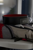 A weightlifting belt with a black exterior and red interior is placed on a surface. Nearby, a gym bag with a mix of gray and red fabric is partially open.