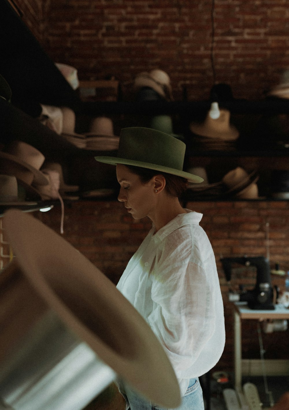 a woman wearing a green hat in a room full of hats