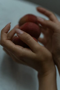 Close-up of a hand holding a peach-colored body lotion with fresh peaches in the background.