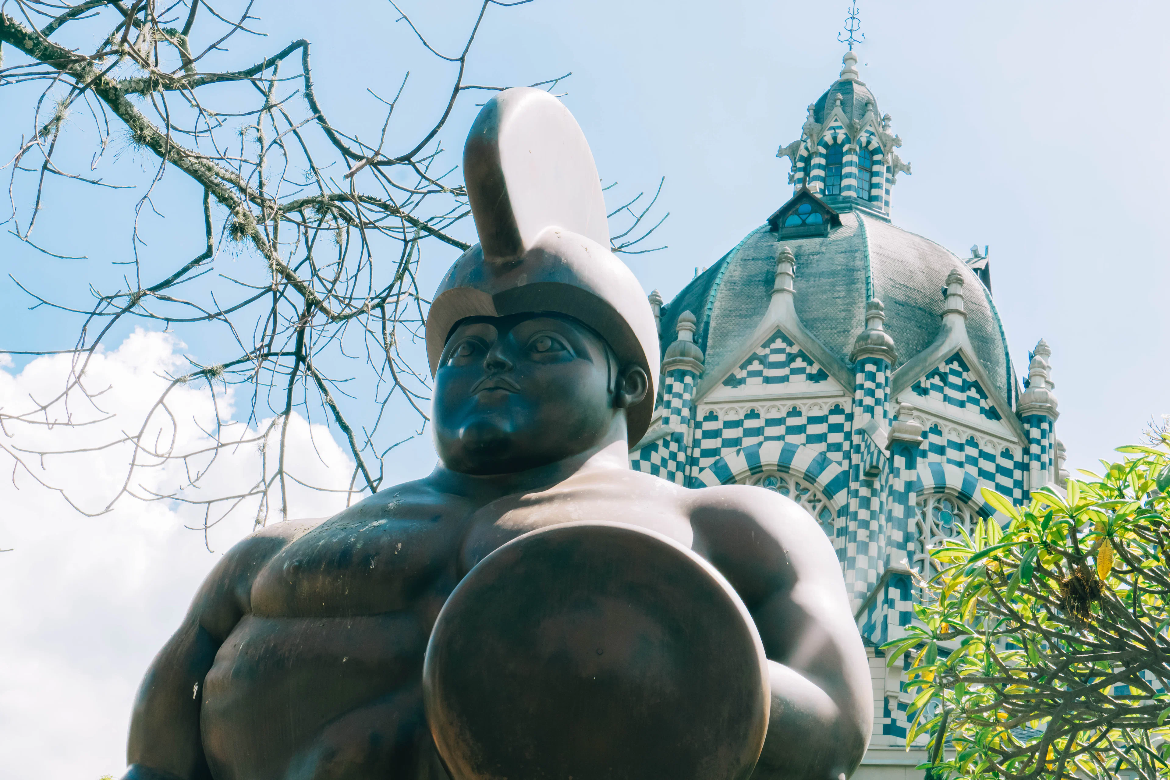 A rounded bronze Botero sculpture in Plaza Botero, with the checkered dome of the Palacio de la Cultura Rafael Uribe Uribe behind it