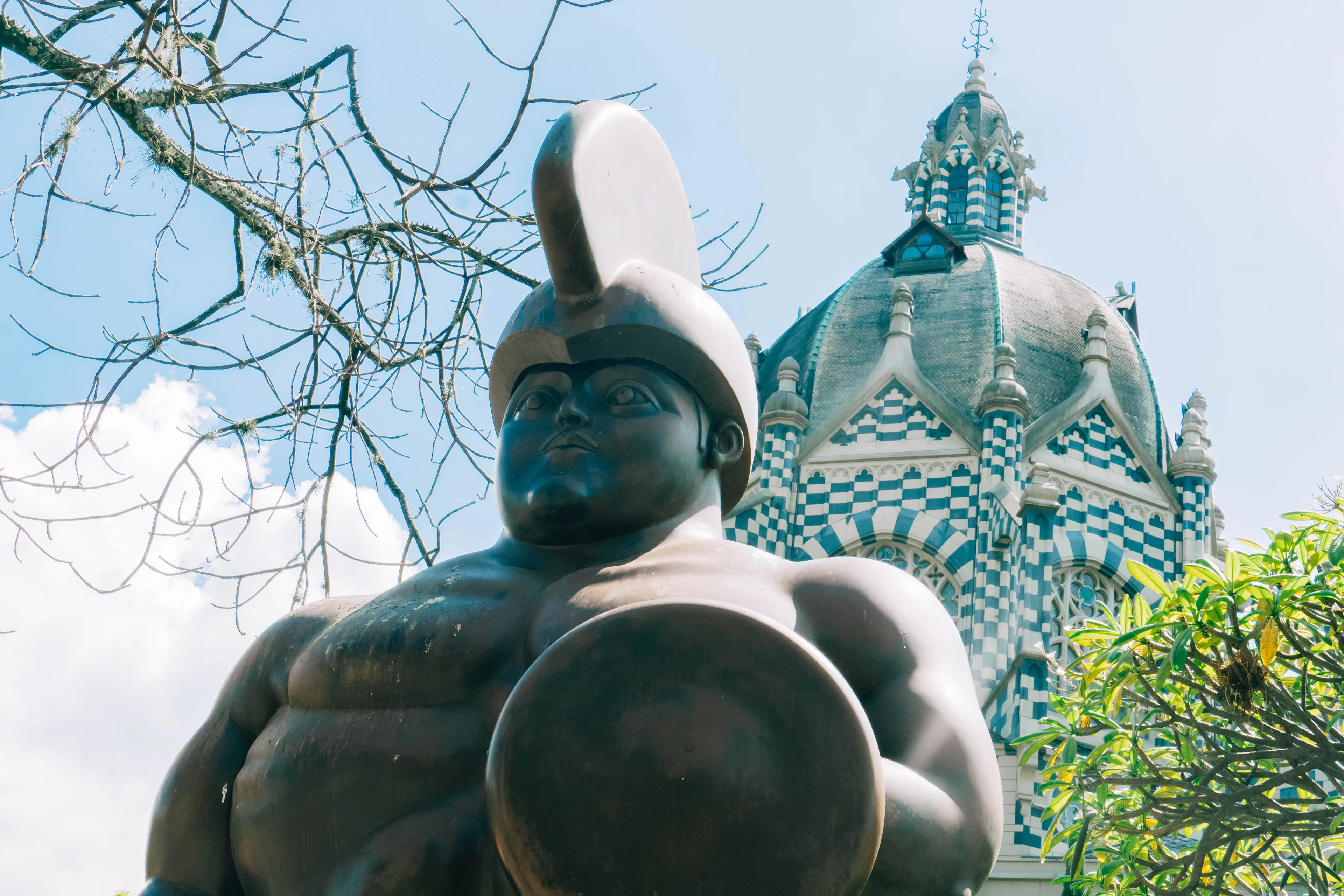 A rounded bronze Botero sculpture in Plaza Botero, with the checkered dome of the Palacio de la Cultura Rafael Uribe Uribe behind it