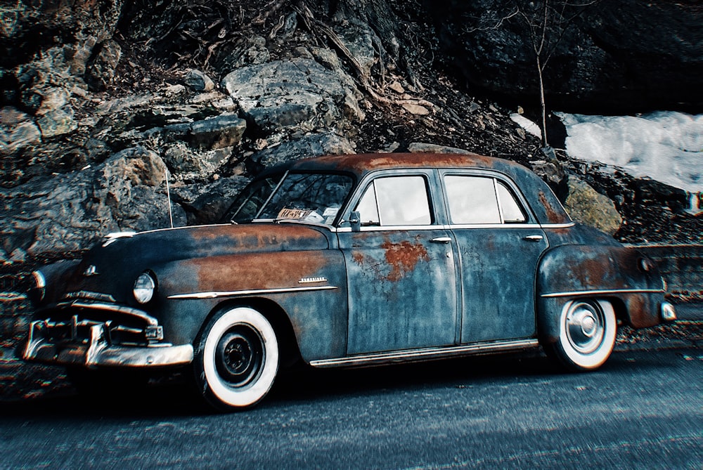 an old rusty car parked on the side of the road