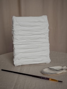 a stack of white cloth sitting next to a paintbrush