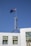 A flag with the British Union Jack and Southern Cross constellation flutters atop a tall metal pole on an architectural structure with white marble tiles against a clear blue sky.