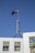 A flag with the British Union Jack and Southern Cross constellation flutters atop a tall metal pole on an architectural structure with white marble tiles against a clear blue sky.