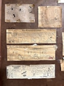 A collection of vintage comic strips from newspapers, including 'Peanuts,' 'Garfield,' and others featuring humorous dialogue and illustrations. The comics are taped onto a brown background, presenting various scenarios involving children, pets, and family life.