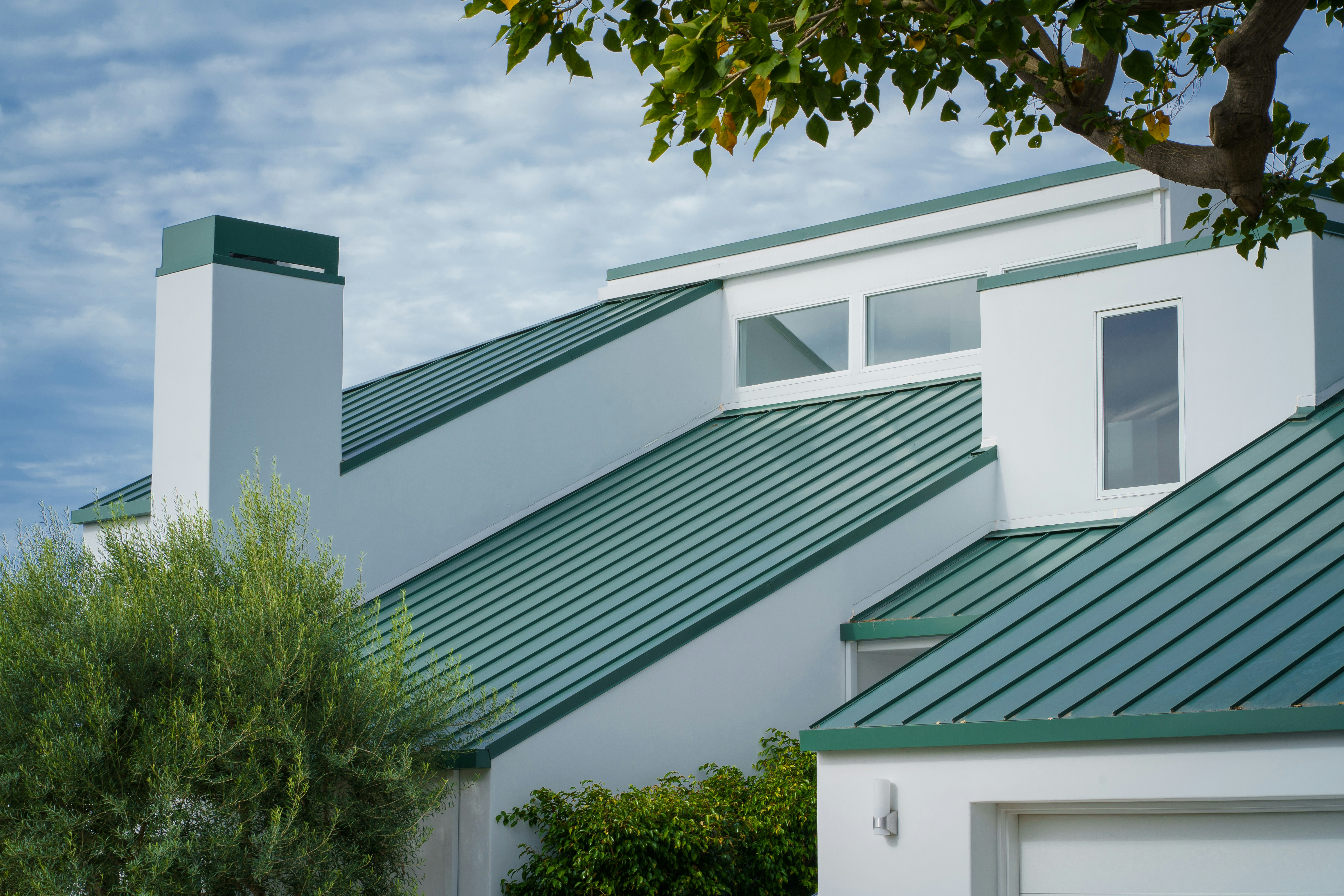 a white house with a green roof and a tree