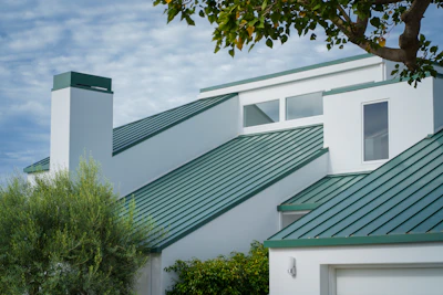 a white house with a green roof and a tree