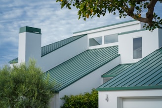 a white house with a green roof and a tree