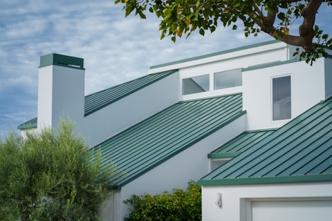 a white house with a green roof and a tree