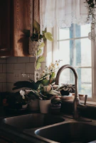 A spacious kitchen sink with a gooseneck faucet surrounded by fresh herbs on the windowsill.