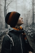 a young boy wearing a hat and scarf in the woods