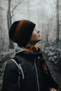 a young boy wearing a hat and scarf in the woods