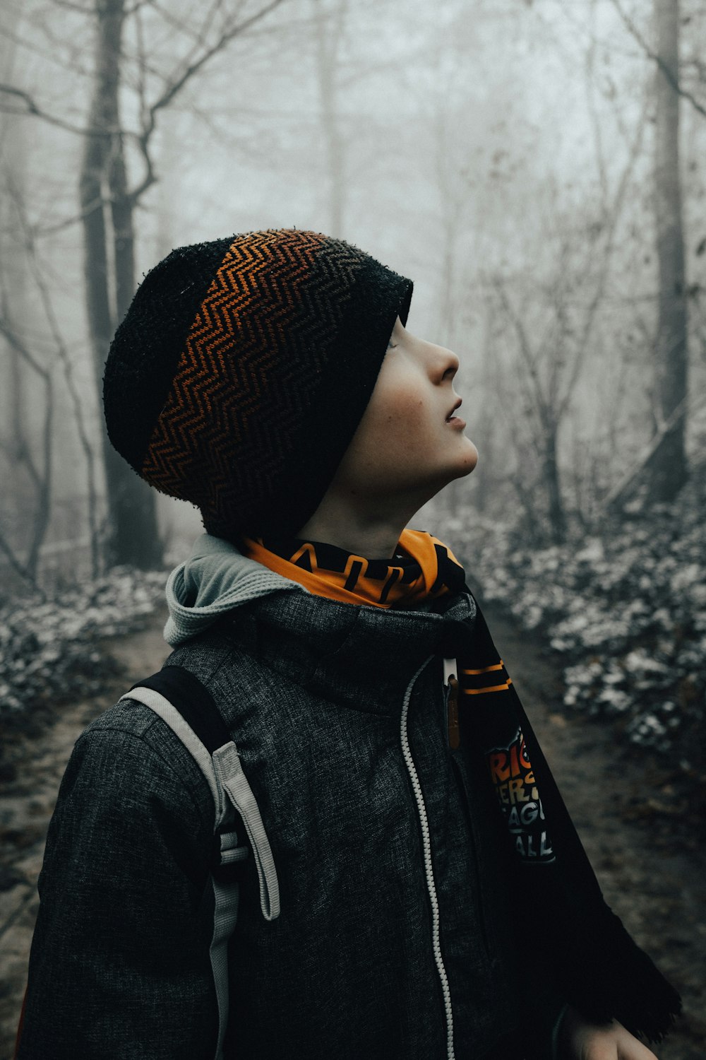 a young boy wearing a hat and scarf in the woods