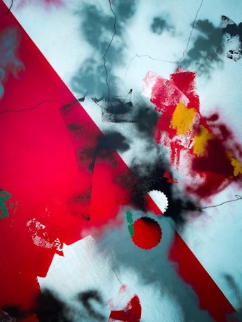 An abstract artwork featuring bold splashes of red, black, and white with hints of yellow and green. The composition includes sharp angles and blurred edges, with various overlapping textures that create a dynamic and chaotic visual effect.