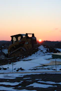 A heavy machinery moving earth on a rural construction site during sunset