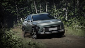A sleek, modern SUV navigates a dirt path surrounded by dense forest. The vehicle is positioned at an angle, highlighting its dynamic design and metallic sheen. Sunlight filters through the trees, casting dappled shadows across the car and the lush greenery.