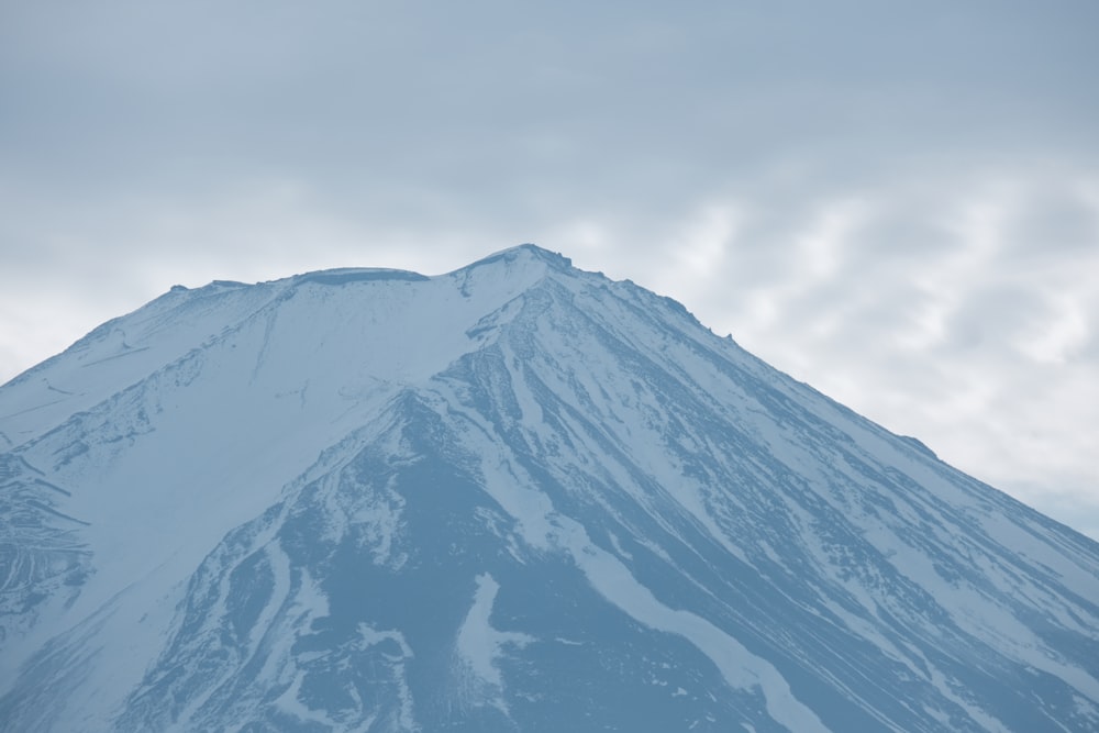 a very tall snow covered mountain under a cloudy sky
