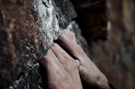 Close-up of climbing hands gripping a rugged rock face with chalk dust in the air.