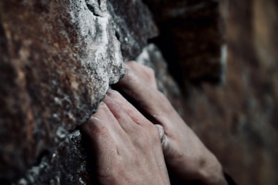 Hands gripping climbing ropes on a rocky cliff face.