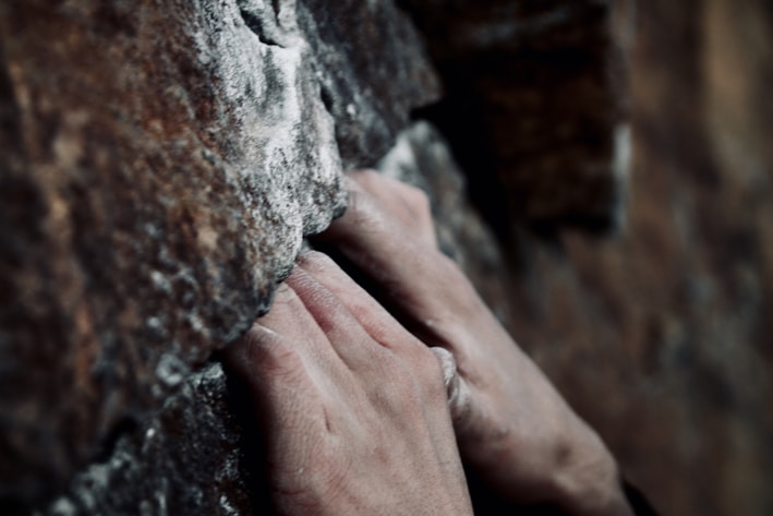 Close-up of rugged climbing gloves gripping a rocky surface under bright sunlight