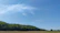 A wide RV site surrounded by lush greenery under a clear blue sky.
