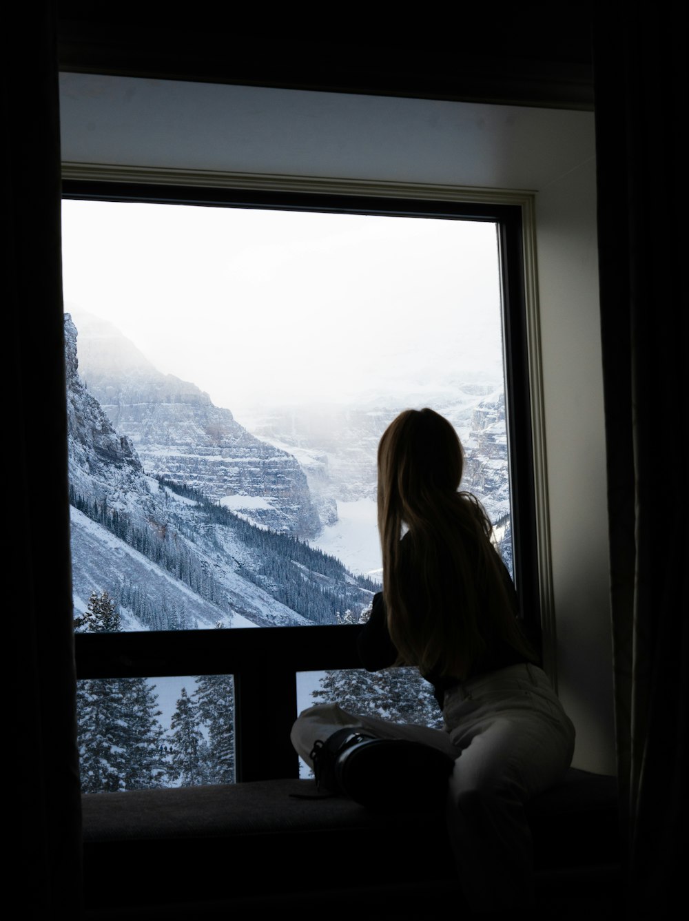 a woman sitting on a window sill looking out a window