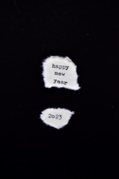 Two pieces of torn white paper are displayed against a black background. The top paper says 'happy new year' and the bottom paper says '2023'.