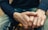 Close-up of a person's hands resting on their lap, featuring a casual attire with a dark sweater and blue jeans.