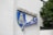 The image features a sign on a building with white textured walls. The sign includes a shield emblem with a stylized portrait of a bearded figure wearing headwear, against a blue background. Above the emblem, the word 'MEDBORGARHUSET' is displayed in uppercase beige letters, and beneath it, the script 'Joar Blå' is written in flowing blue cursive letters. Green leaves from a tree partially cover the right side of the building.