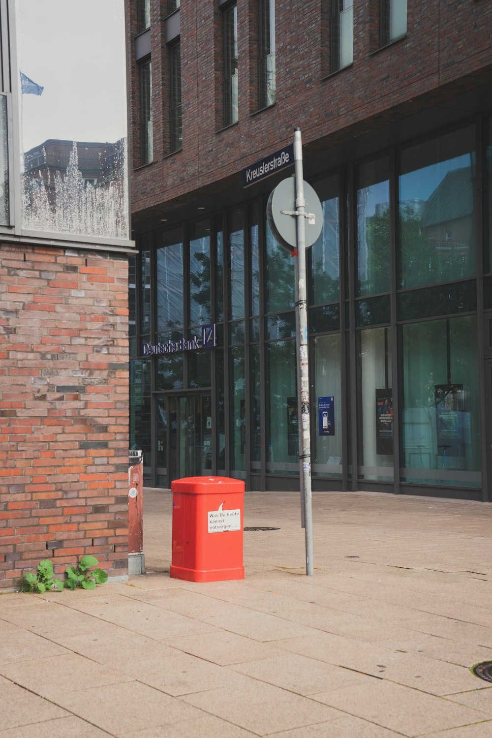 a red trash can sitting in front of a tall building