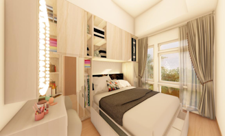 A cozy bedroom features a neatly made bed with a grey blanket and patterned pillows. Above the bed, there are wooden storage cabinets with various items, including folded clothes and decorative pieces. The room is adorned with soft, flowing curtains and has a dressing table with makeup items neatly arranged beside a large mirror surrounded by warm lights.