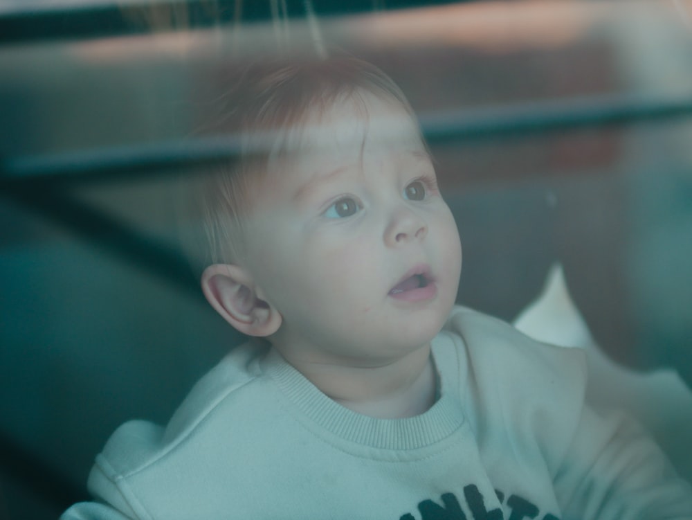 a little boy sitting in a car seat looking out the window