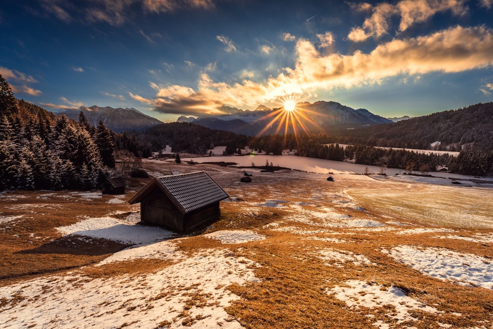 the sun is setting over a small cabin in the mountains