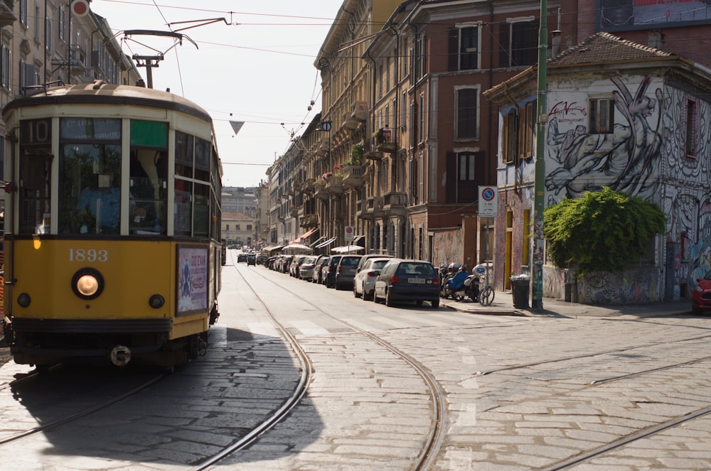 a yellow trolley car traveling down a street next to tall buildings