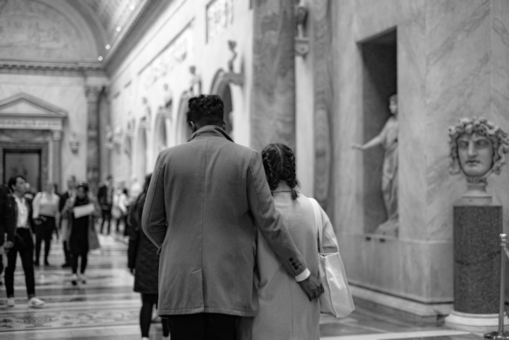 a black and white photo of a man and a woman walking through a building
