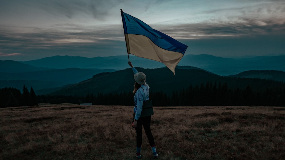 a woman standing on top of a grass covered field holding a flag