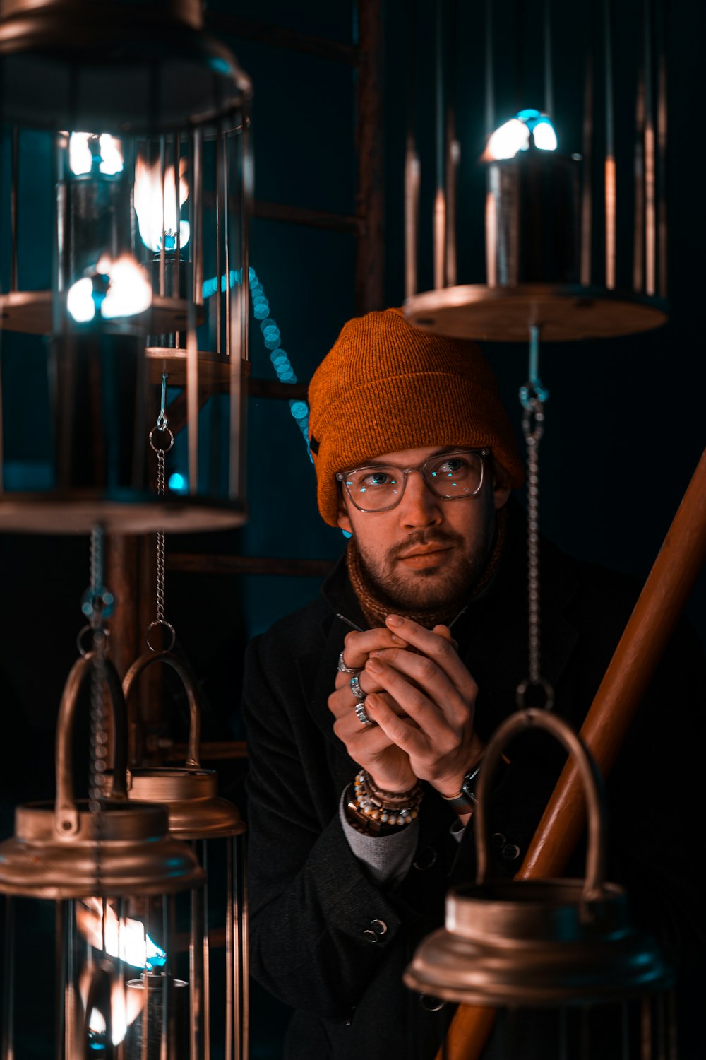 a man wearing a hat and glasses standing in front of a chandelier